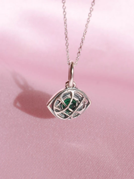 Silver pendant with green gemstone on a pink fabric background