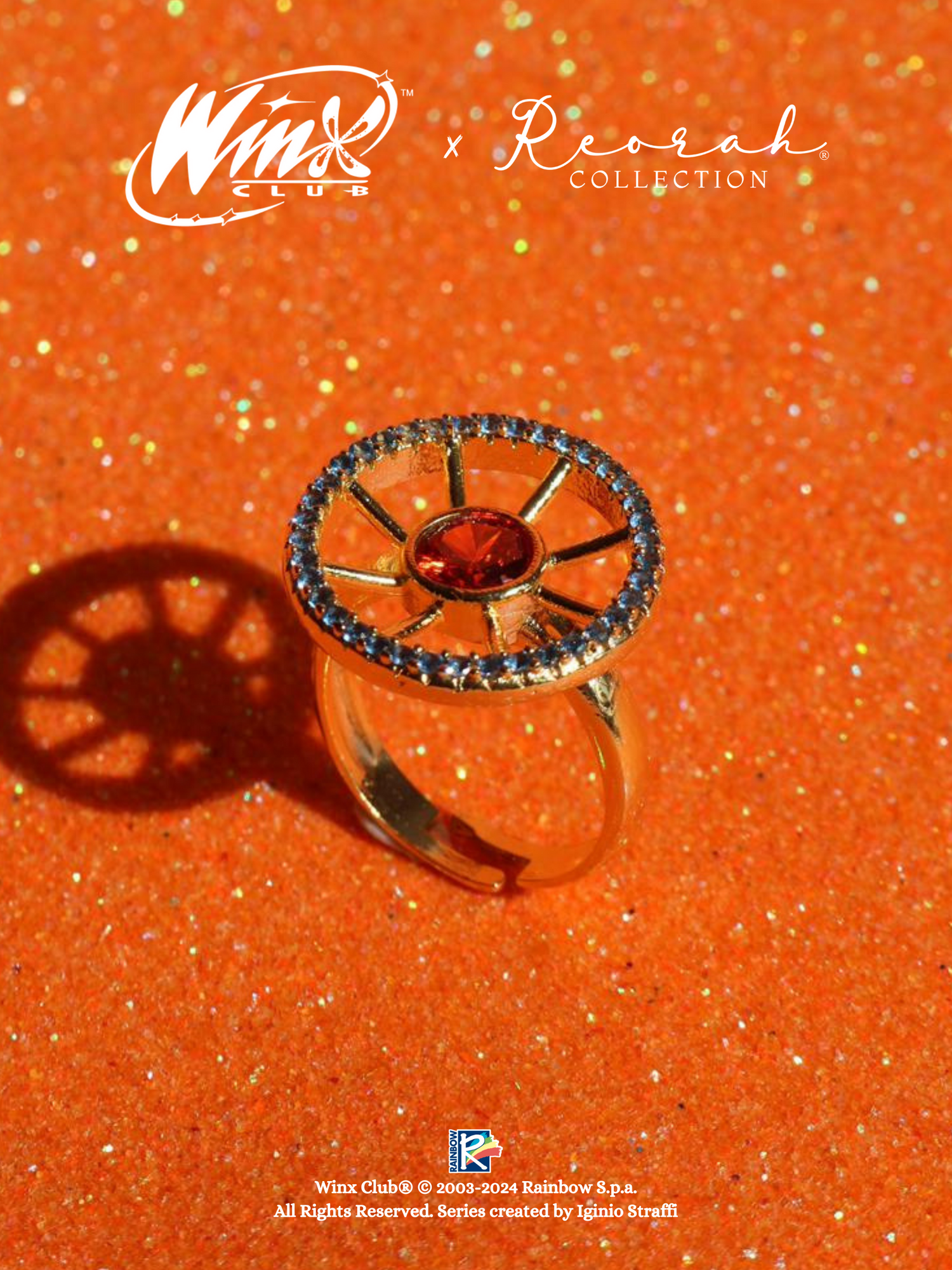 An official Winx Club Ring of Solaria with a red central zirconia stone surrounded by blue stones on a orange glittery background.