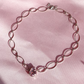 A silver-plated choker necklace with a link chain design and a central pink zirconia stone, displayed on a pink background.