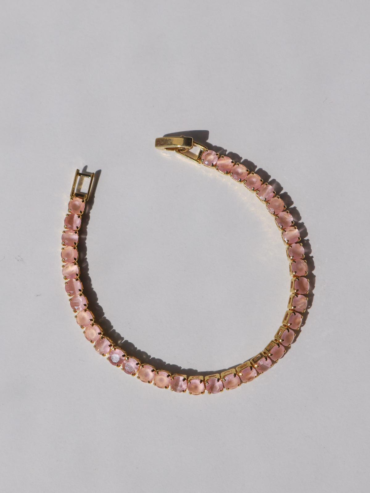 A bracelet with icy pink zirconia stones set in brass, displayed against a white background.