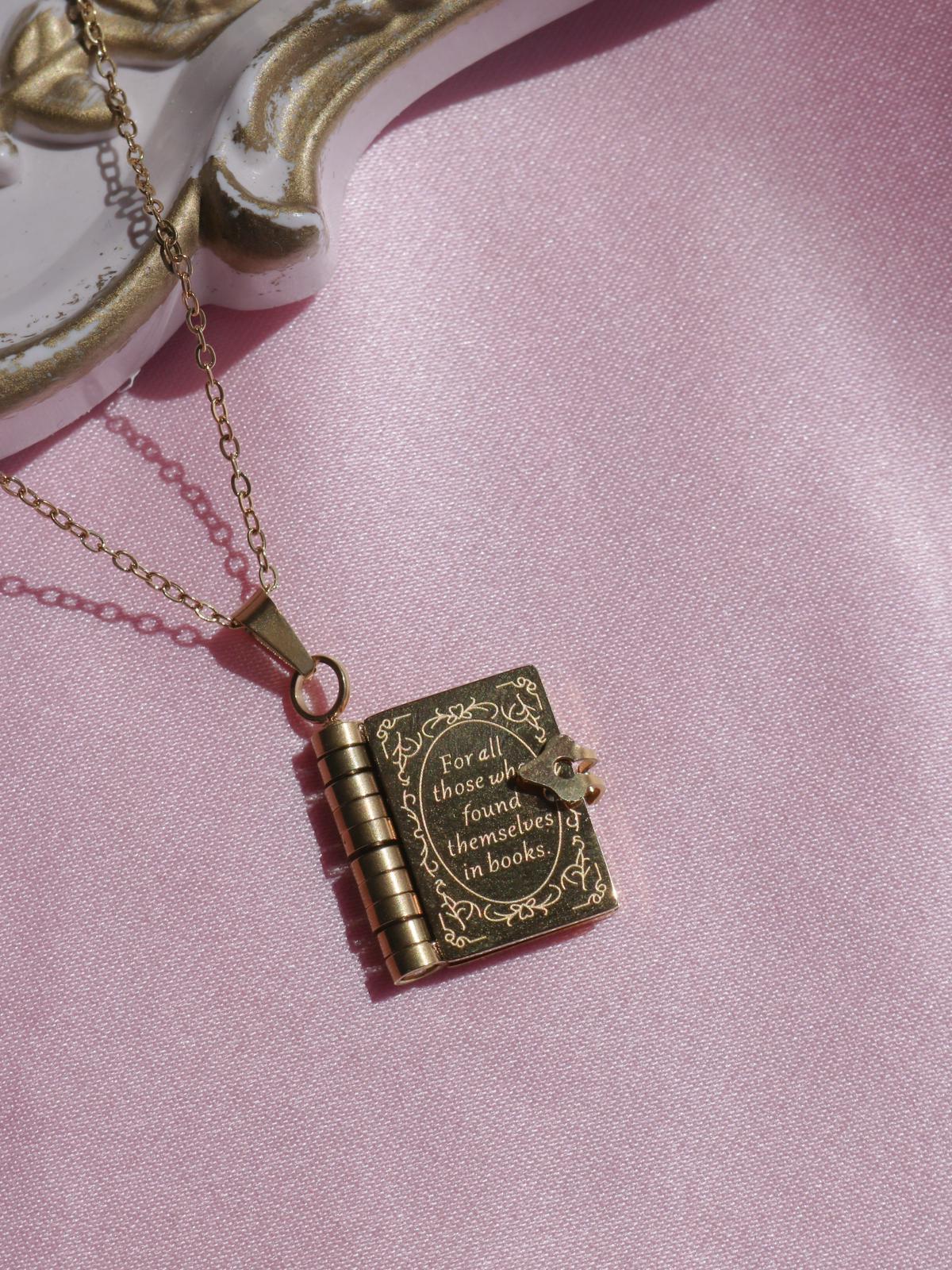 A stainless steel necklace with a book-shaped pendant on a pink background.