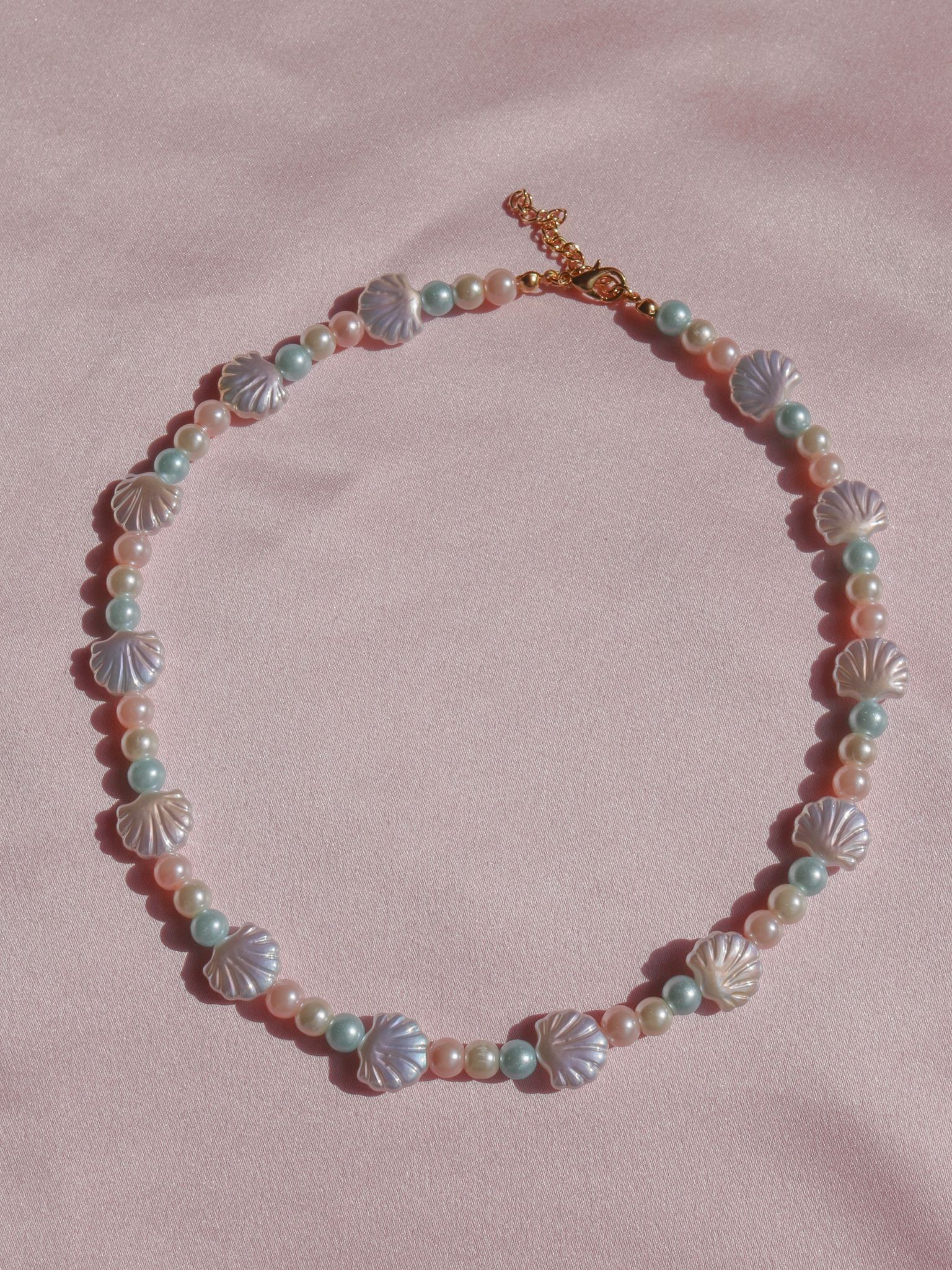 A brass necklace featuring glass pearl stones with a variety of colors, displayed on a pink background.