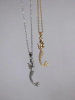 Two mermaid-themed necklaces, one with a silver mermaid figure attached to a chain and another with a gold mermaid figure attached to a chain.