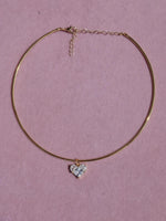 Gold necklace with a heart-shaped pendant on a pink background