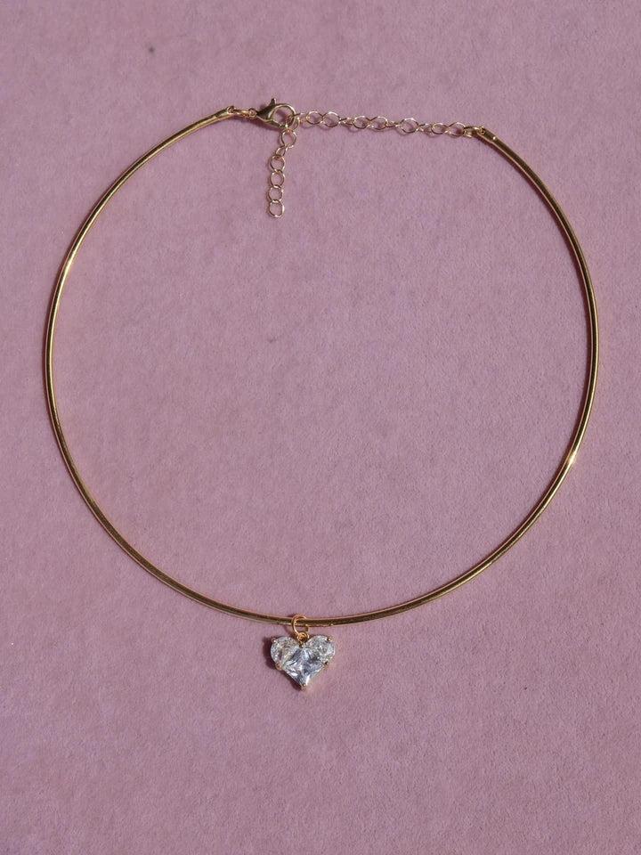 Gold necklace with a heart-shaped pendant on a pink background