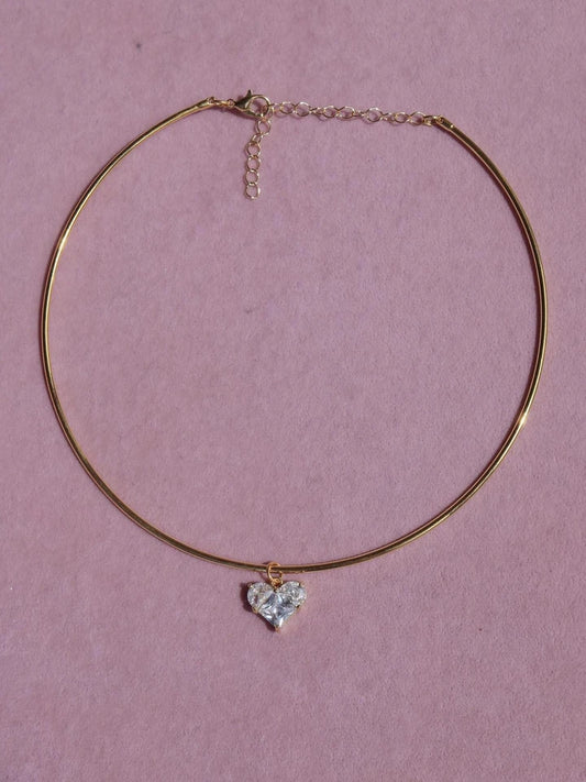 Gold necklace with a heart-shaped pendant on a pink background