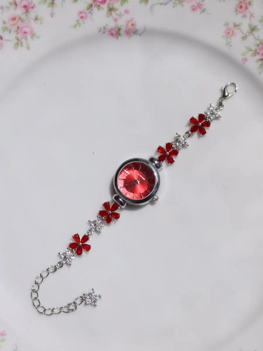 A silver-tone charm bracelet with red crystal flowers and a large round red crystal centerpiece, displayed on a white plate with a pink floral border.