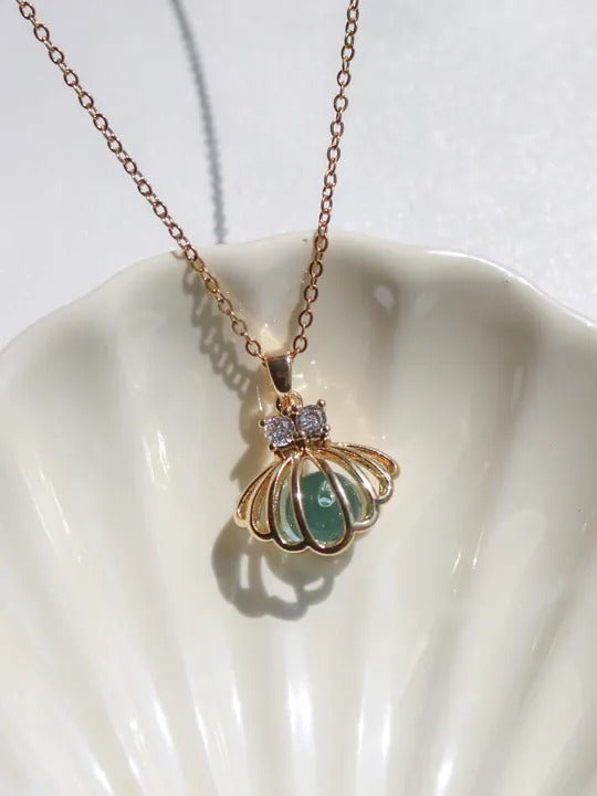 Gold necklace with a green gemstone pendant on a white shell background