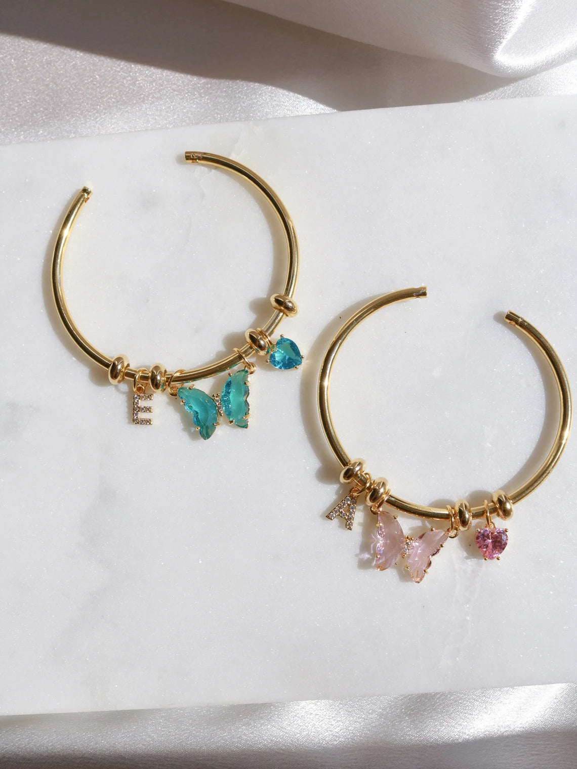 Two gold-colored friendship bracelets with charms, displayed on a white surface.